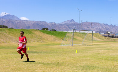 Man sprinting across soccer training field past metal goalpost with yellow cones, copy space