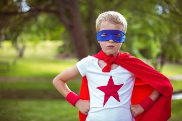 Papier peint photo Child standing confidently in grassy park wearing red cape and wristbands with blue eye mask