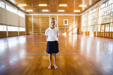 Girl standing barefoot and wearing PE uniform in school gym, with polished floor and climbing racks