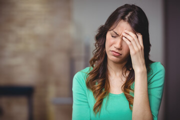 Woman in twenties pressing her temple at home with brick accent wall, grey wall, copy space