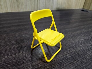 Bright yellow plastic chair placed on dark wood table, highlighting contrast, suitable for modern...