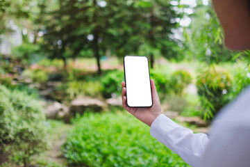 Mockup image of a woman holding mobile phone with blank white desktop screen in the nature outdoors