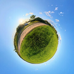 Creative tiny planet image with a rural road, car, sunset, and lush green fields wrapped into a...