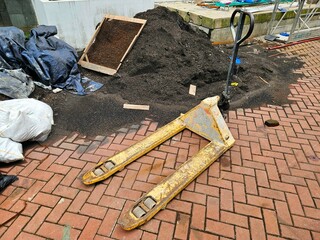 Rusty hand pallet jack placed on brick surface surrounded by work debris, suitable for construction...
