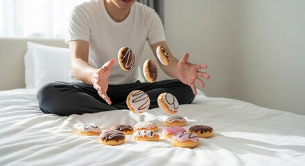 Young asian adult male tossing colorful donuts on bed in bright room