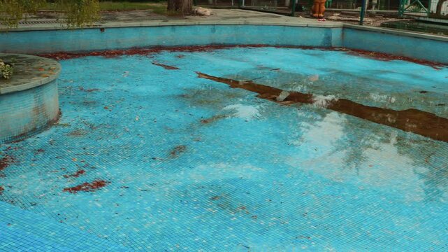 View of an empty dirty swimming pool with leaves and debris during the off-season. Pool and backyard maintenance. Pan shot