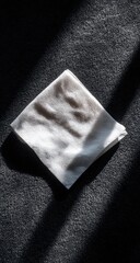 A folded, off-white cloth rests on a dark surface, illuminated by angled light