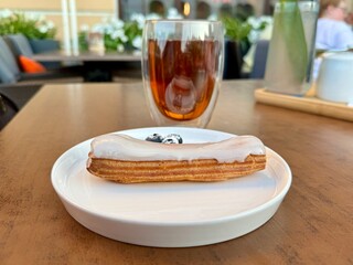 Creamy mouth-watering eclair with a cup of tea for dessert in a summer cafe. High quality photo
