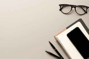 Top view flat lay showing modern minimalist office stationery including an open notebook, black pen and stylish glasses neatly arranged on a matte grey background.