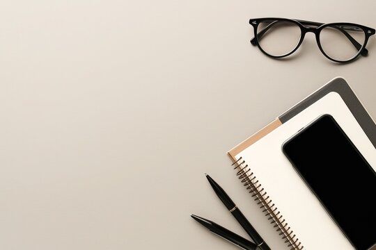 Top view flat lay showing modern minimalist office stationery including an open notebook, black pen and stylish glasses neatly arranged on a matte grey background.