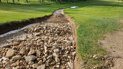 Streambed lined with stones on golf course after rainfall enhances natural drainage in lush green landscape concept