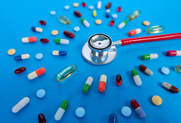 Stethoscope surrounded by various capsules and tablets on a bright blue background representing healthcare and medicine concept