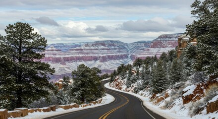 A winding road descends into a snow-dusted canyon, revealing layered rock formations under a cloudy sky (1)