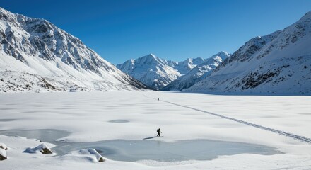 Winter Landscape of a Person Walking Across a Snowy Valley Surrounded by Snow Covered Mountains Under a Clear Blue Sky