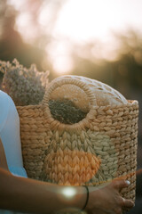 Woman carries a woven basket filled with bread and herbs during sunset outdoors