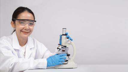 A smiling woman in lab attire is using a microscope, showcasing a scientific environment focused on...