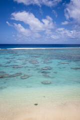 Beautiful aqua blue ocean water covering a shallow tropical reef under a cloudy blue sky. Captured from the idyllic sandy shoreline.