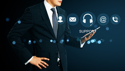 Businessman holding tablet with digital customer support icons on dark background representing virtual online help and communication network.