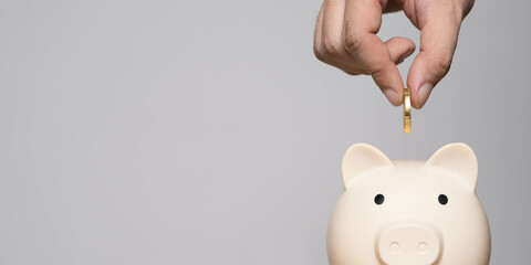A hand is dropping a coin into a piggy bank, symbolizing saving money and financial planning.