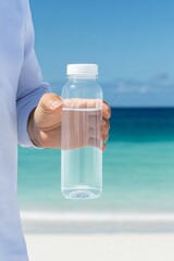 Man’s hand holding a clear plastic bottle of water against turquoise ocean, symbol of purity and lifestyle