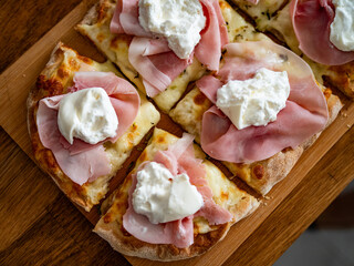 Pinsa romana with boiled ham and burrata cheese on wooden board, close-up