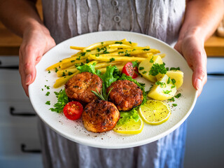 Woman holding plate with fried chicken meatballs with boiled potatoes and wax beans, close-up