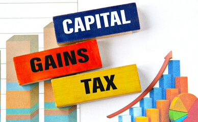 CAPITAL GAINS TAX - words on multi-colored wooden blocks on the background of charts