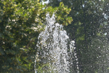 Close-up of water splashing from fountain with sunlit droplets against green background