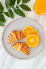 Elegant breakfast flat lay with croissants, orange slices, and fresh juice on marble table, bright orange and yellow tones, aesthetic composition with green sprig