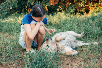 girl petting dog lying on its back in grass backyard scene summer day peaceful atmosphere golden...
