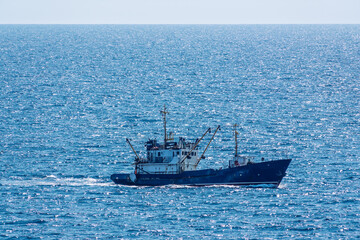 Fishing boat in blue sea and clear sky with birds flying overhead.