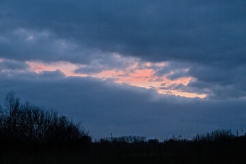  Evening cloudscape witb dark blue rainclouds and orange glow over a wetlands landscape in...