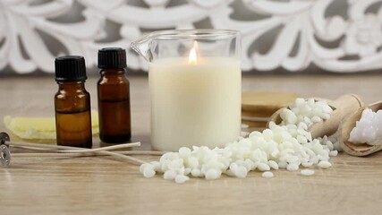 Concept of making scented homemade massage oil candle. Tools, materials on table fragrance oil bottles, glass jar with pouring spout, coconut wax, soy wax flakes, candle wicks on table. 