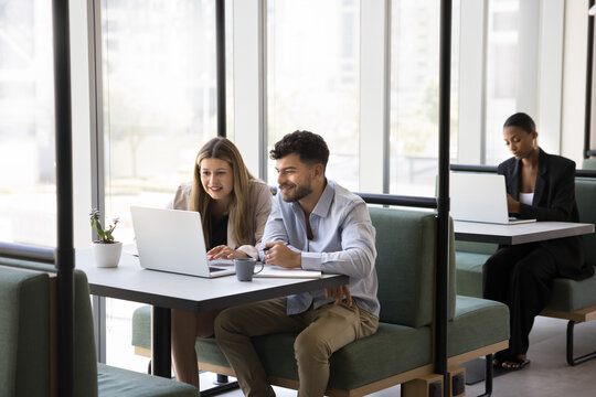 Modern work culture. Businesspeople of different ethnic backgrounds sit at comfortable tables in coworking area use personal notebooks individually or in teams create ideas in productive atmosphere