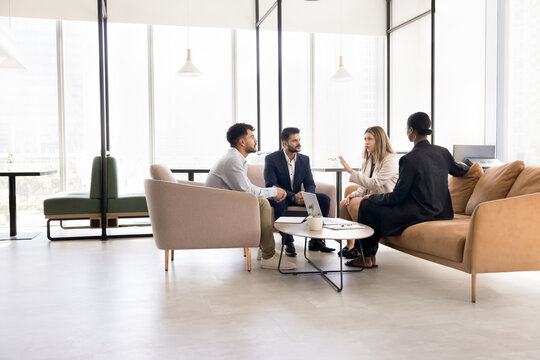 Business partners coworkers of diverse ethnicities meet for informal team briefing in cozy shared workspace hold brainstorming session talk discuss project paperwork collaborate on ideas. Copy space