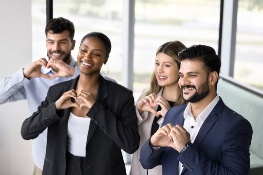 Unity in diversity. Multiethnic group of diverse business professionals stand together smile make heart shapes with fingers as symbol of collaborative spirit warm relationship team friendship support