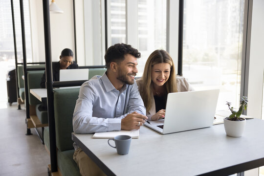 Professional collaboration in comfy environment. Happy smiling pair of diverse businesspeople startup developers project creators work together in glass cabin of modern coworking area using notebook