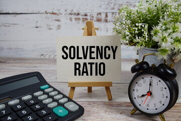 Solvency Ratio text with alarm clock and calculator on wooden background