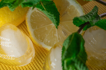 Refreshing summer close-up of lemon slices, mint leaves, and round ice cubes on a yellow...