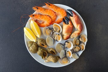 Delicious seafood platter featuring a variety of shellfish including shrimp, crab claws, clams, and mollusks served as a takeaway meal on a rustic table setting with ample space for food photography