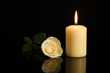 Close-up of a lit candle reflected on a dark mirror surface with a somber theme