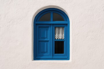 Fototapeta premium Classic blue wooden window with an arch, set against a textured white wall