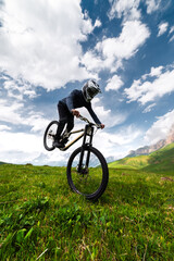mountain biker takes off with his rear wheel leaning on his front wheel, performing a manuel or...