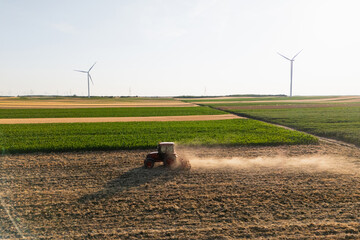 Agricultural tractor is working on the field with wind turbines
