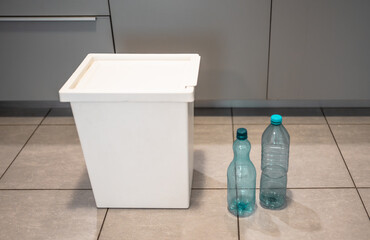 Plastic bottles next to a trash bin. Sorting plastic for easier recycling of waste.