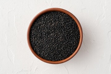 Close-up of black sesame seeds in a ceramic bowl on a white textured surface from a top perspective