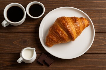 Freshly baked croissant served on a plate atop a rustic wooden surface, perfect for breakfast. Top-down view.