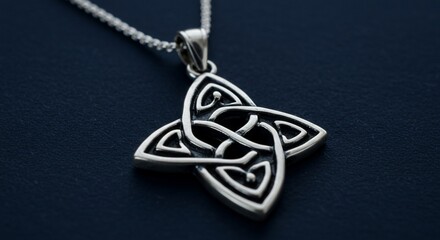 Silver Celtic Knot Pendant on Chain, Close-Up Detail on Dark Blue Surface