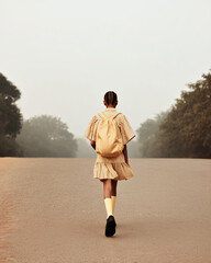 Young girl walking alone on empty road with school backpack