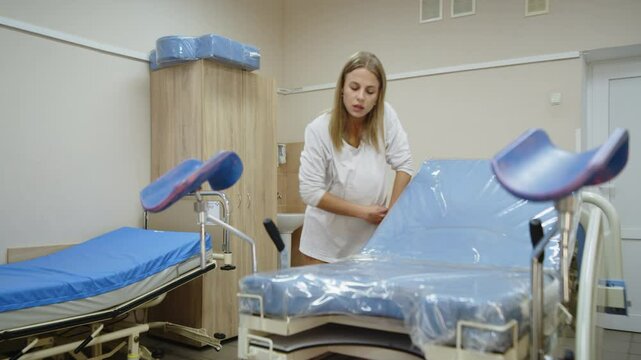 Pregnant woman experiencing painful contractions before labor. She leans on a gynecological chair in a hospital room. Concept support and labor preparation